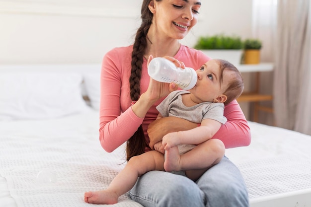 Cura del bambino Mamma amorevole che dà bottiglia con acqua o latte alla sua piccola figlia mentre si rilassa insieme sullo spazio della copia del letto