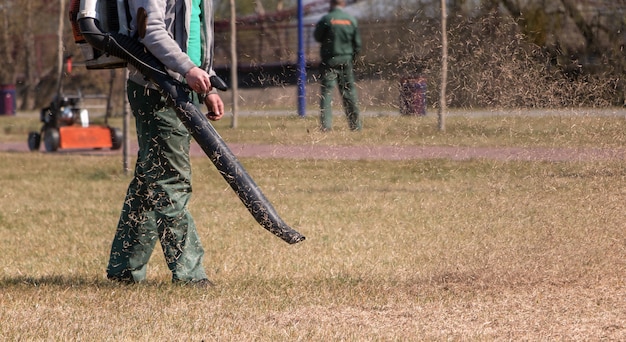 Cura del prato. Il giardiniere rimuove la vecchia erba secca dal prato del parco con un soffiatore portatile a benzina.