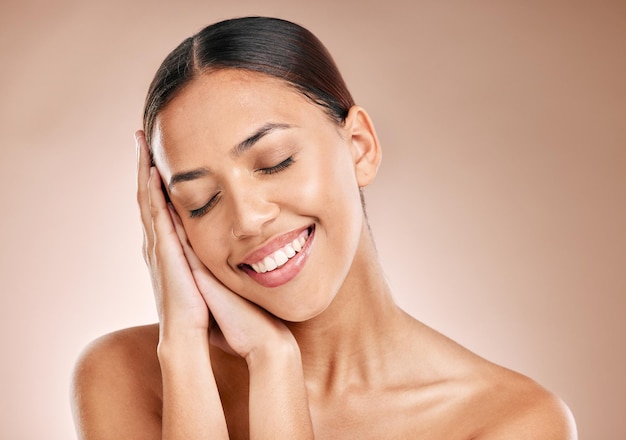 Cura della pelle bellezza e relax donna con gli occhi chiusi e sorriso sullo sfondo dello studio Trucco glamour e cura della pelle di lusso con le mani sul bel viso cosmetici naturali per il viso disintossicante sulla donna felice