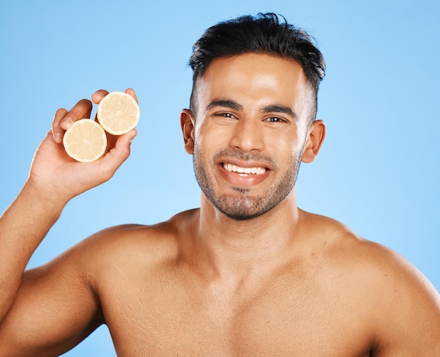 Cura della pelle del viso e arancione con un modello di uomo in studio su sfondo blu per promuovere la bellezza naturale Ritratto di frutta e benessere con un bel giovane maschio in posa per un prodotto o un trattamento per la salute