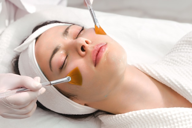 Cura della pelle del viso una maschera viene applicata al viso di una donna in una clinica di cosmetologia da vicino