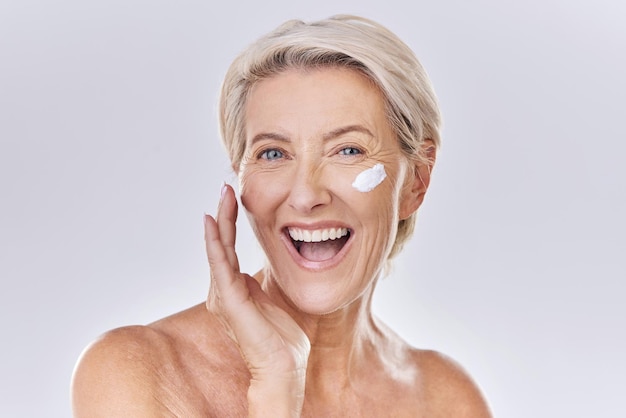 Cura della pelle di bellezza e benessere con una donna anziana che applica crema solare o siero lozione sul viso in studio su sfondo grigio Cura della pelle sanitaria e motivazione con un modello bello e sano