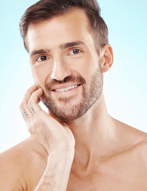 Cura della pelle e ritratto di un bell'uomo isolato su uno sfondo blu in studio Bellezza pulita e volto di un modello sorridente per cosmetici dermatologia bagliore e cosmetologia su uno sfondo
