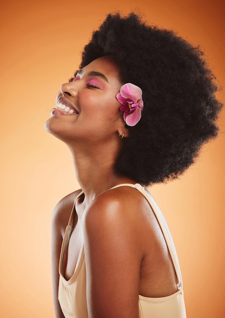 Cura della pelle e trucco di bellezza con una donna nera modello in studio su uno sfondo arancione con un afro e un sorriso Capelli del viso e felice con una giovane donna attraente in posa per cosmetici o benessere