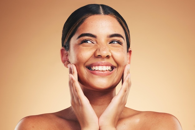 Cura della pelle felice e mani sul viso naturale della donna in studio per il benessere cosmetico o la dermatologia su sfondo marrone Sorriso di bellezza e modello entusiasti per risultati di pelle luminosa o cosmetologia dell'amore per se stessi