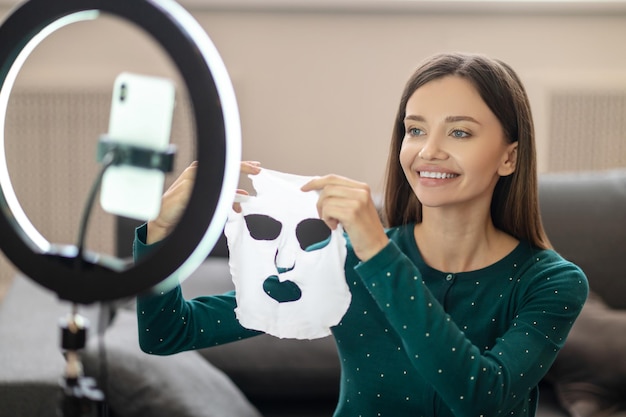 Cura della pelle. Giovane donna che dimostra una maschera idratante durante il tutorial online