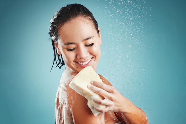 Cura della pelle in studio e donna in doccia con spugna isolata su sfondo blu mockup Pulizia con spruzzi d'acqua o sana igiene del modello femminile che fa il bagno o fa la doccia per la bellezza e la cura del corpo