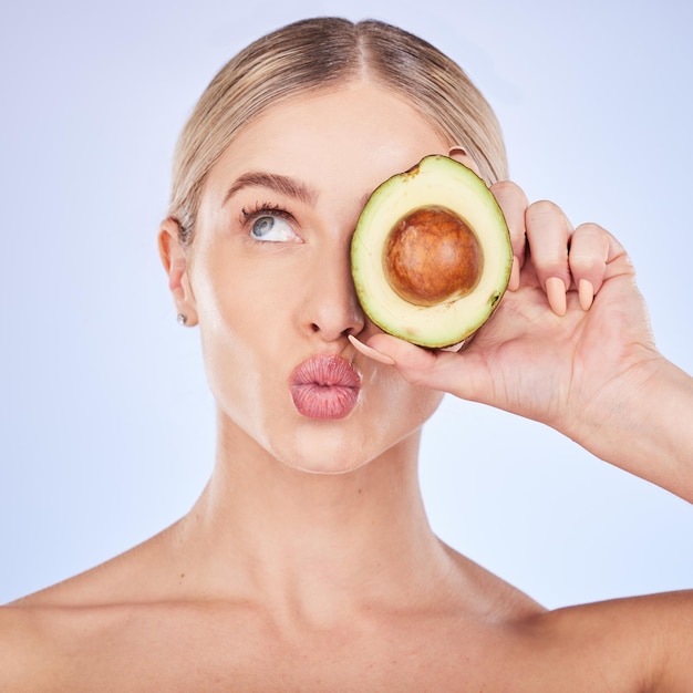 Cura della pelle viso e donna con avocado in studio isolato su sfondo blu Cosmetici bacio frutta e pensiero modello femminile con cibo per omega 3 nutrizione o dieta pelle sana o broncio di bellezza