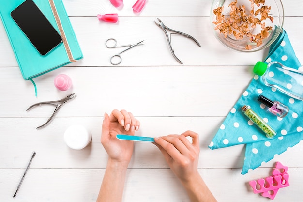 Cura delle mani della donna. Vista dall'alto delle mani della bella donna liscia con strumenti professionali per la cura delle unghie per manicure su sfondo bianco. Avvicinamento. Vista dall'alto. Copia spazio