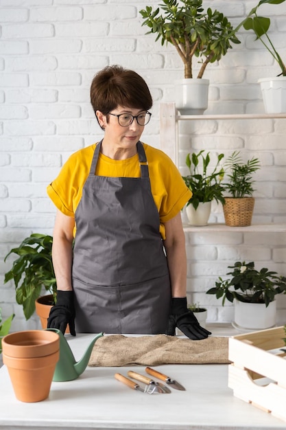 Cura delle piante d'appartamento primaverili Rinvaso delle piante d'appartamento Svegliare le piante d'appartamento per la primavera Una donna di mezza età sta trapiantando una pianta in un nuovo vaso a casa Pianta da trapianto di giardiniere Spathiphyllum