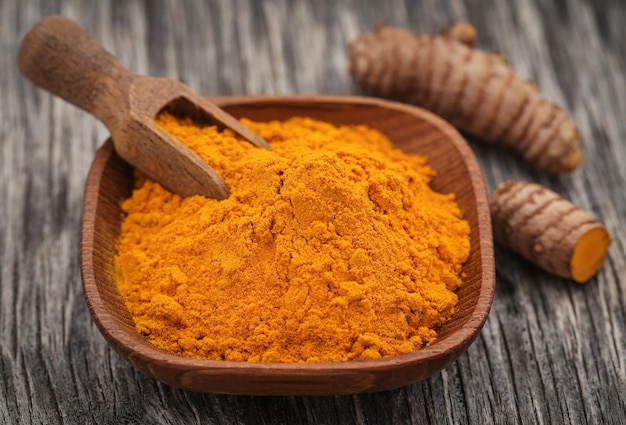 Curcuma cruda con polvere in una ciotola di legno