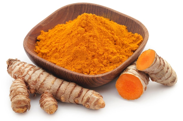 Curcuma cruda con polvere in una ciotola su sfondo bianco