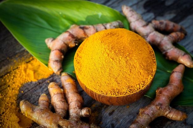 Curcuma in polvere e curcuma fresca in ciotole di legno con foglia verde sul vecchio tavolo di legno Le erbe sono originarie del sud-est asiatico