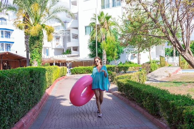 Cure ragazza sta andando in spiaggia con un cerchio gonfiabile e ascoltando musica in cuffia sul suo telefono