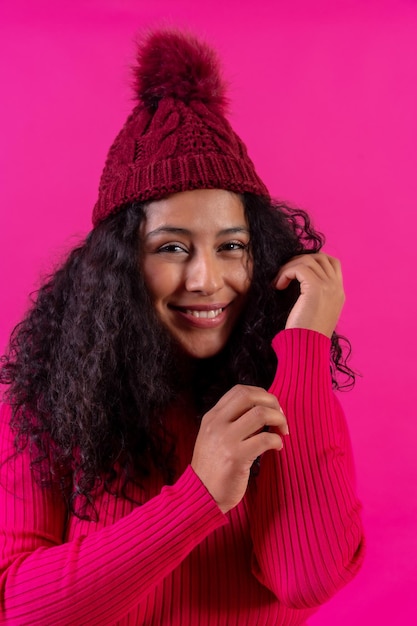 Curlyhaired donna in un berretto di lana su uno sfondo rosa ritratto sorridente girato in studio