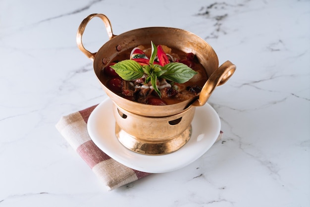 Curry d'anatra arrosto al litchi in un piatto di stufato di rame isolato su vista dall'alto opaco su sfondo di marmo grigio