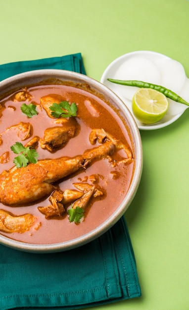 Curry di pollo rossastro piccante o Masala, con un pezzo di gamba prominente, servito in una ciotola o Kadhai su sfondo colorato o in legno. messa a fuoco selettiva.