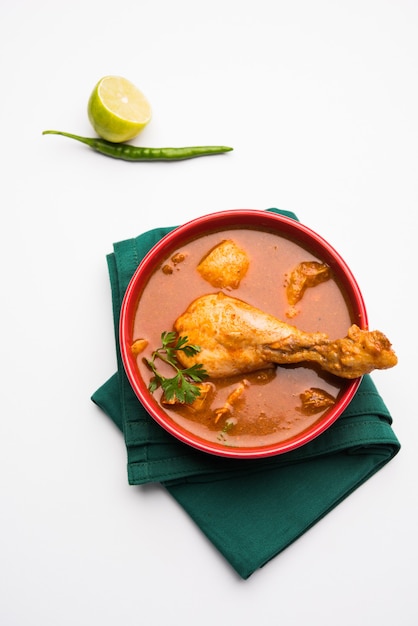 Curry di pollo rossastro piccante o Masala, con un pezzo di gamba prominente, servito in una ciotola o Kadhai su sfondo colorato o in legno. messa a fuoco selettiva.