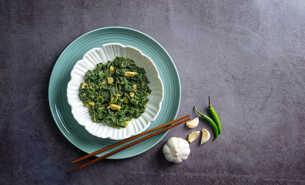 curry di spinaci in ciotola bianca e piatto blu con peperoncino spicchio d'aglio bacchette su piastrelle di ardesia nera vista dall'alto