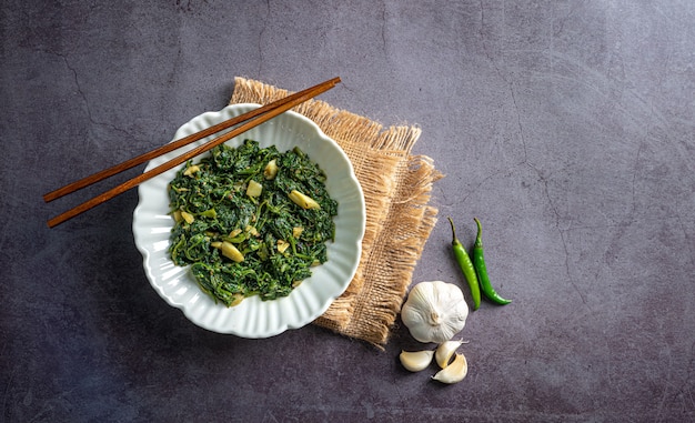 curry di spinaci in ciotola bianca su piastrella di ardesia nera con uno strato vintage bacchette spicchio d'aglio e peperoncini vista dall'alto