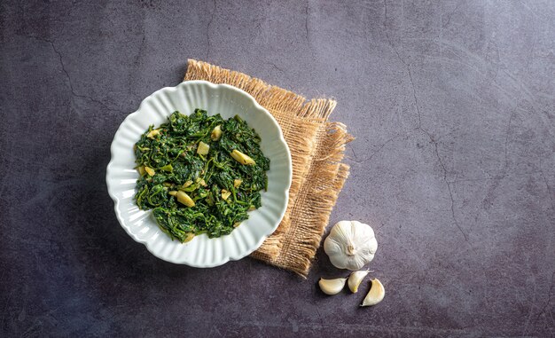 curry di spinaci in ciotola bianca su piastrella di ardesia nera con uno strato vintage e vista dall'alto di spicchio d'aglio