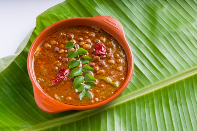 Curry Kadala o curry chana masala o curry di ceci disposti in terracotta su una foglia di banana verde fresca con sfondo bianco.