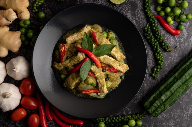 Curry verde di maiale in piatto nero con spezie su uno sfondo di cemento nero