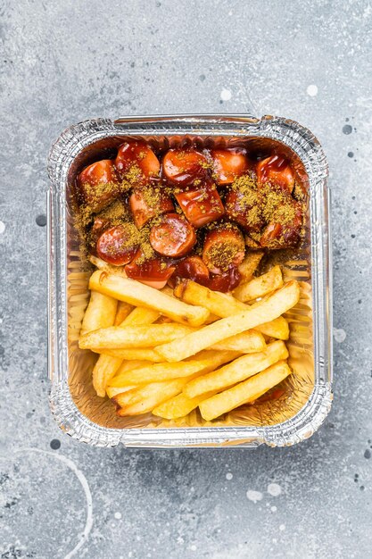 Currywurst tedesco tradizionale con patatine fritte servite da asporto Sfondo grigio Vista dall'alto