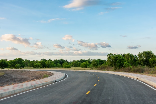 Curva vuota della strada asfaltata e cielo blu pulito nel fondo di giorno di estate con lo spazio della copia