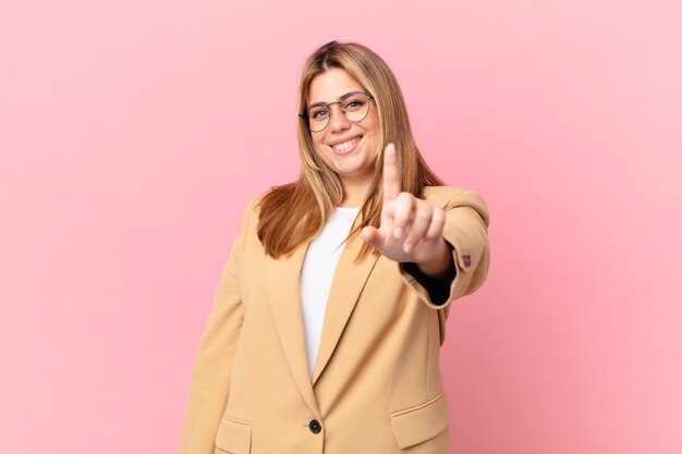 Curvy bella donna bionda che sorride con orgoglio e sicurezza facendo il numero uno