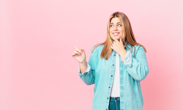 Curvy bella donna bionda che sorride con un'espressione felice e sicura con la mano sul mento