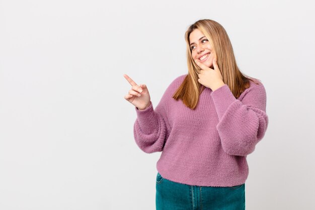 Curvy bella donna bionda che sorride con un'espressione felice e sicura con la mano sul mento