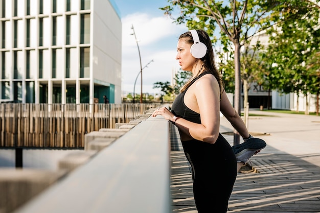 Curvy giovane donna atletica che si allunga mentre si ascolta musica all'aperto