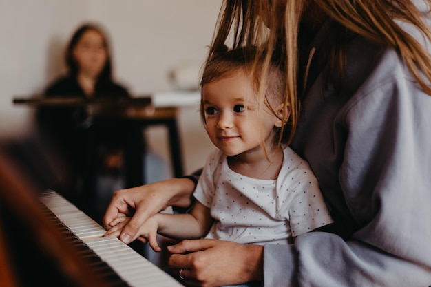 Cute bambina felice che suona il pianoforte in una stanza luminosa Effetto rumore di messa a fuoco selettiva