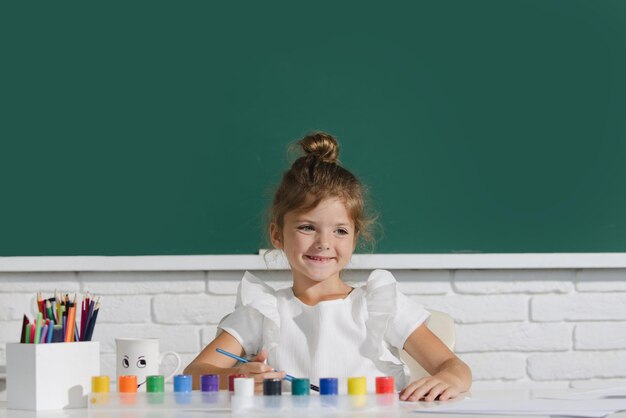 Cute bambina pittura con colori vernici e pennello Ragazza carina della scuola che disegna in classe a scuola