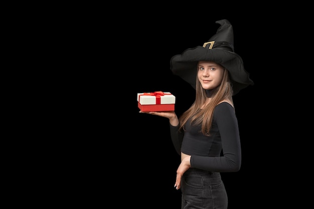 Cute giovane donna in cappello nero strega con regalo sul palmo Ragazza su sfondo nero Copia spazio