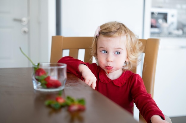 Cute little caucasica bionda baby girltoddler prettyadorable infant mangiare fragola dal tavolo dentro