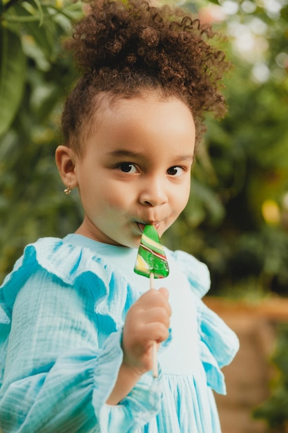 Cute little swarthy girl mangiare lecca-lecca a forma di anguria Bambino con lecca-lecca nel giardino botanico