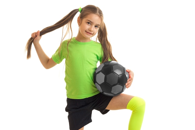 Cutie bambina gioca a calcio e guarda la telecamera isolata su sfondo bianco