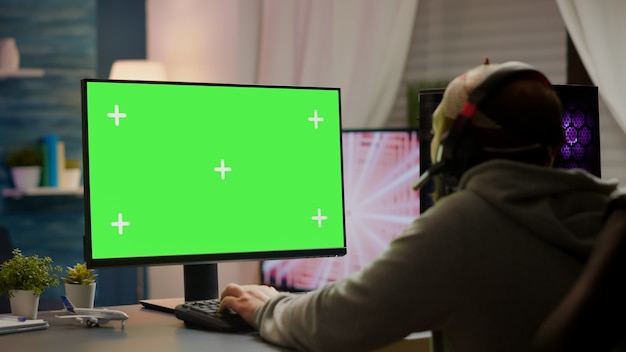 Cyber gamer professionista che gioca ai videogiochi con greenscreen, chroma key, mock up display desktop isolato. Giocatore che utilizza un computer potente con giochi sparatutto in streaming su schermo mockup che indossano le cuffie