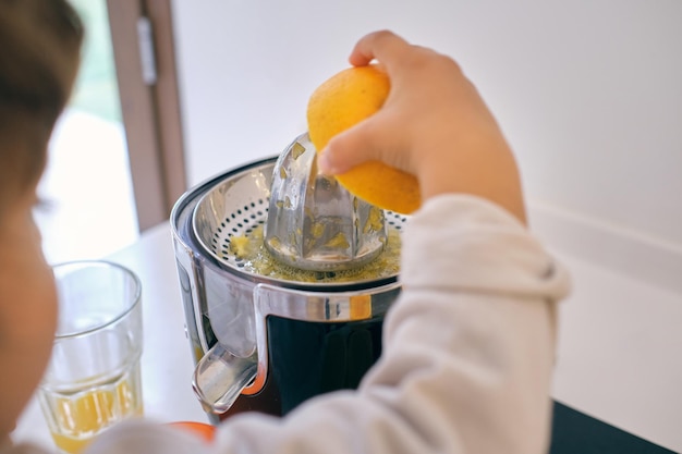 Da sopra del raccolto bambino anonimo che prepara succo d'arancia fresco per una colazione sana in cucina a casa