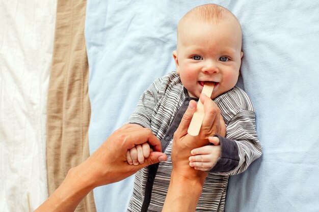 Da sopra la donna del raccolto che controlla bocca del bambino adorabile sveglio con il bastone di legno che si trova sul plaid