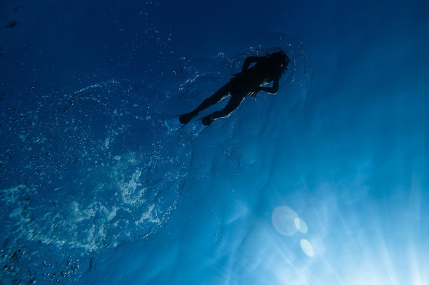 Da sotto di un subacqueo a corpo intero anonimo in tuta da bagno e pinne in maschera da snorkeling che galleggia nell'acqua blu del mare in una giornata estiva