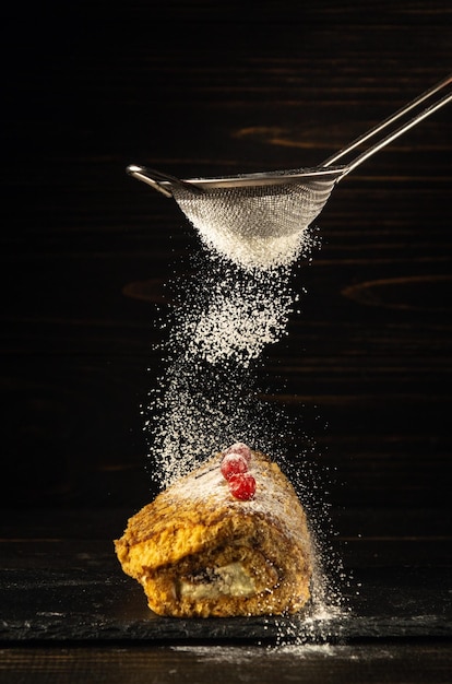 Da un setaccio su una torta al forno con bacche rosse cospargere di zucchero a velo Delizioso concetto di dessert su sfondo nero