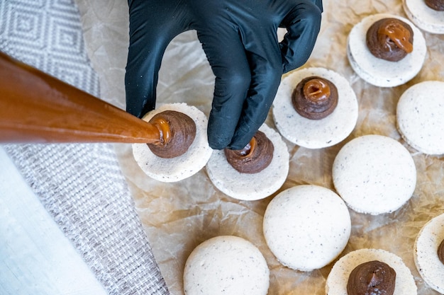 Da una tasca da pasticcere spremere la crema al cioccolato su metà degli amaretti a fuoco selettivo clouse up