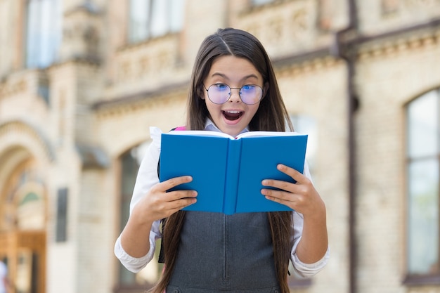 Dai un'occhiata, leggi un libro. Il bambino felice ha letto il libro all'aperto. Biblioteca scolastica. Educazione all'alfabetizzazione. Lista di lettura. Imparare a leggere. Lettura casalinga. Lezione di letteratura. Corsi di lingua straniera.