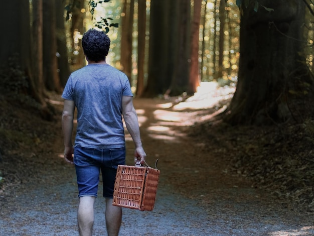 Dal retro cammina lungo un sentiero tra gli alberi in un parco pubblico con un cesto di vimini