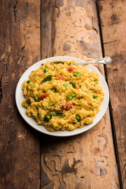 Dalia di verdure o Daliya Khichadi o Khichdi di grano spezzato con pomodoro, piselli e peperoncino, servito in una ciotola o in un piatto
