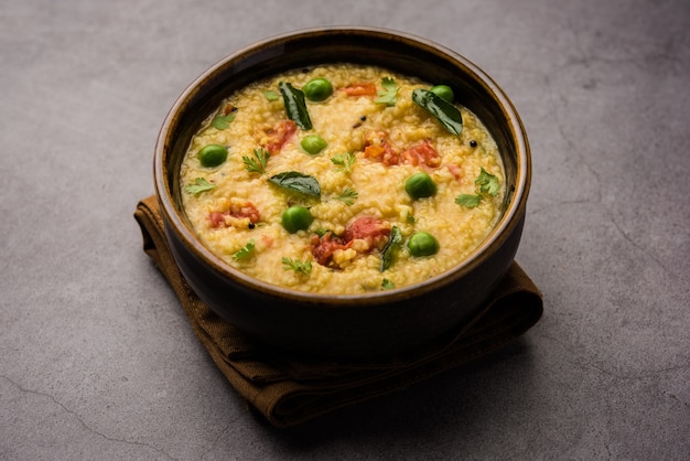 Dalia di verdure o Daliya Khichadi o Khichdi di grano spezzato con pomodoro, piselli e peperoncino, servito in una ciotola o in un piatto