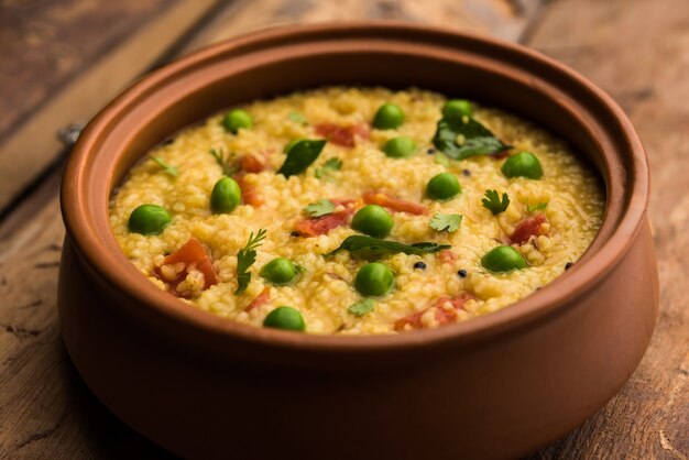 Dalia di verdure o Daliya Khichadi o Khichdi di grano spezzato con pomodoro, piselli e peperoncino, servito in una ciotola o in un piatto